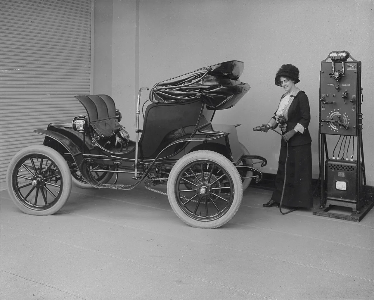 General Electric'in 1912 tarihli tanıtım fotoğrafında şık giyimli bir kadın, elektrikli otomobilini ev tipi doğrultucuya bağlıyor